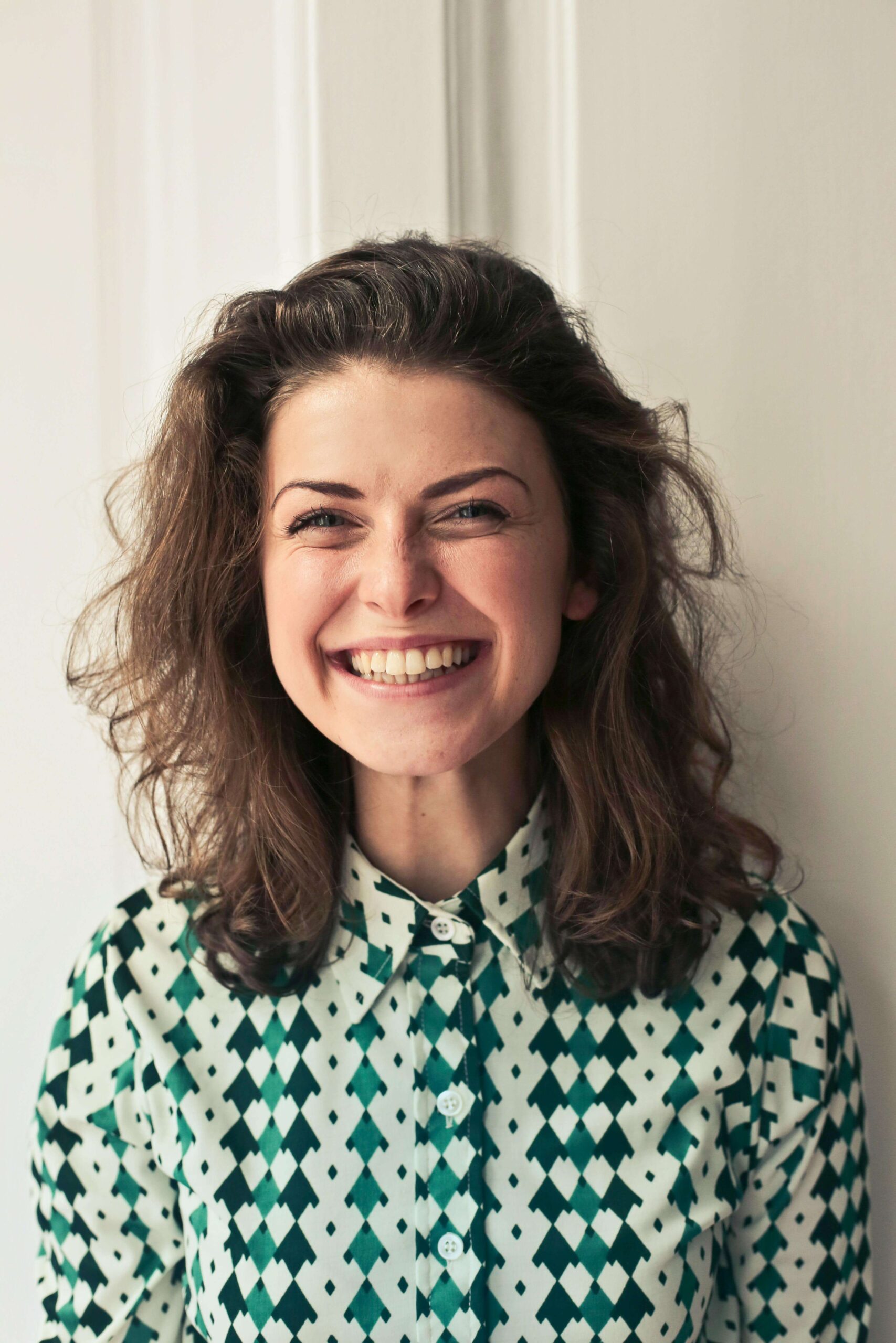 A smiling woman with curly hair, wearing a patterned shirt, exuding satisfaction and happiness