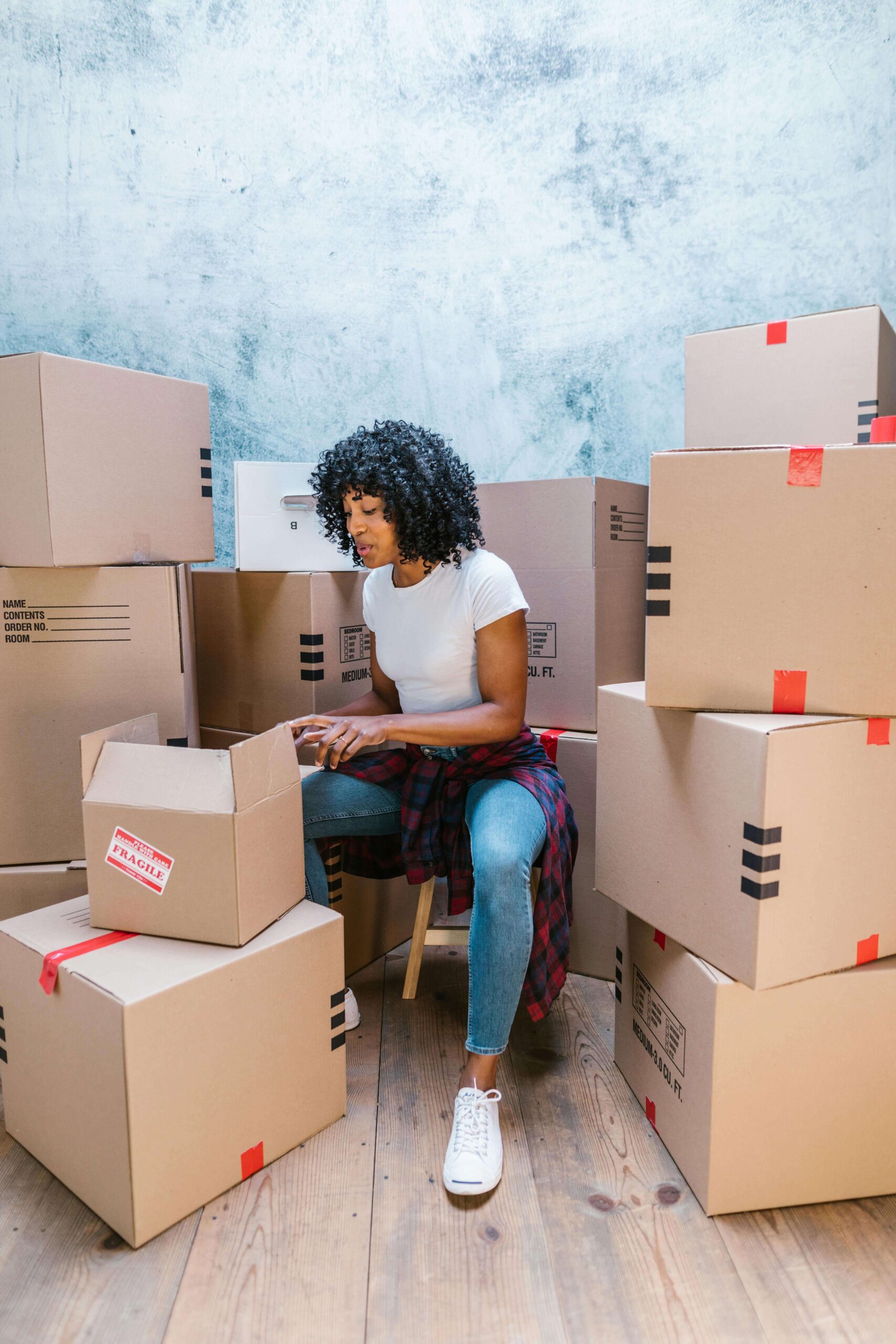 A woman sitting amidst a number of packed moving boxes, possibly planning her office relocation