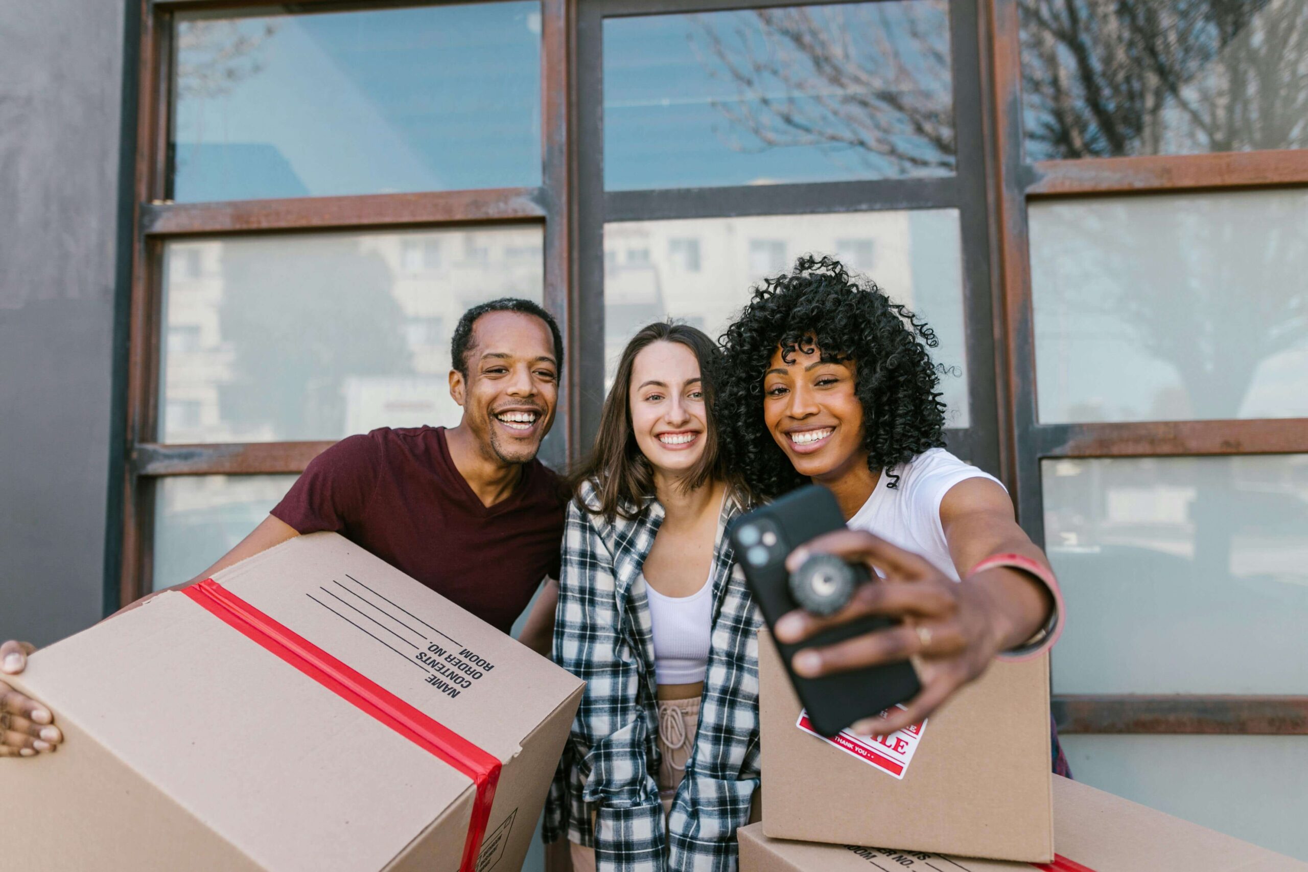 Three cheerful colleagues taking a selfie with moving boxes, celebrating a successful office relocation.