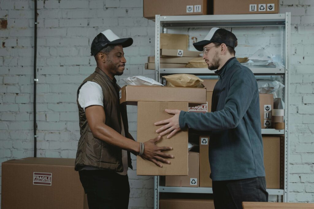 Two workers at a storage service facility handling a cardboard box marked as fragile