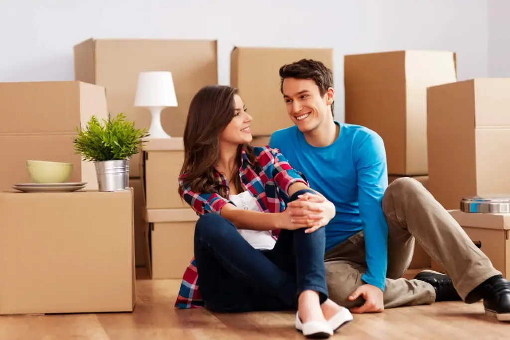 Happy couple sitting on the floor among moving boxes in their new home in Sydney