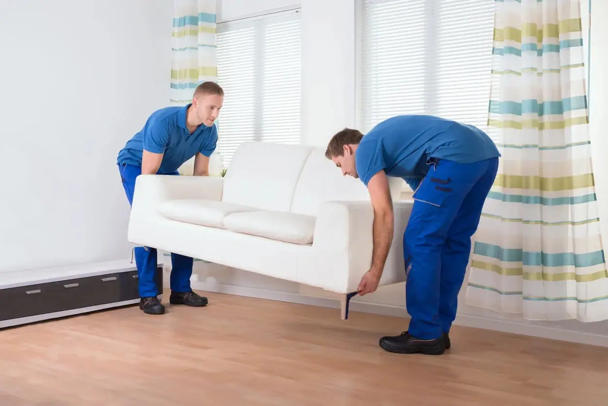 Two professional movers carefully lifting a white couch to relocate in a Sydney home